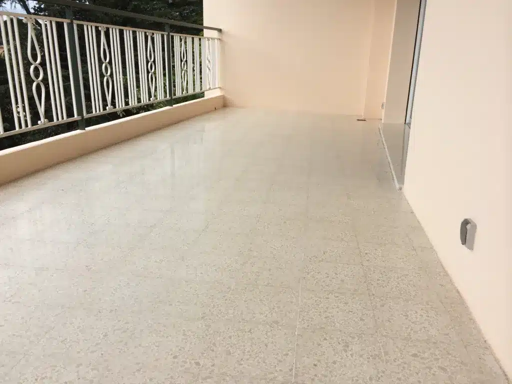 poncage-granito-poli-satine-le-cannet Terrasse en granito d'un immeuble du Cannet après ponçage, avec une finition poli-satiné, la balustrade à gauche et la porte-fenêtre à droite