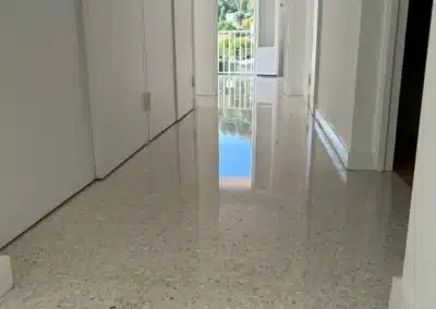 Couloir d'un appartement de Grasse avec un sol en granito poli-brillant reflétant la porte-fenêtre ouverte au fond