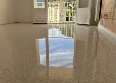 Chambre d'un appartement de Grasse avec un sol en granito poli-brillant reflétant la porte-fenêtre, le balcon et le ciel, avec vue sur les immeubles voisins