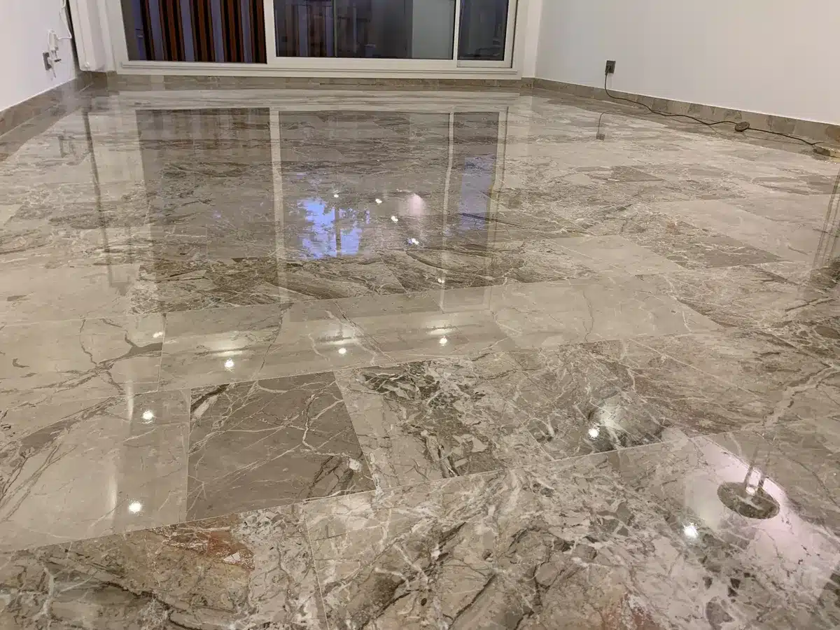 marbre-breccia-poli-brillant-reflet-baie-sejour-mandelieu Séjour d'un appartement de Mandelieu-la-Napoule avec un sol en marbre Breccia poli-brillant reflétant la baie vitrée et une lampe