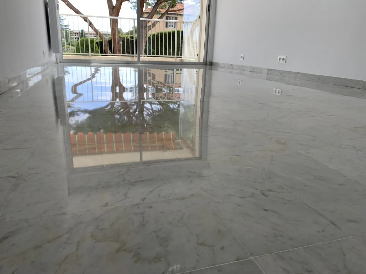 marbre-gris-clair-veine-poli-brillant-chambre-reflet-baie-golfe-juan Chambre d'un appartement de Golfe-Juan avec un sol en marbre veiné gris clair poli-brillant, reflétant la baie vitrée et les arbres du balcon