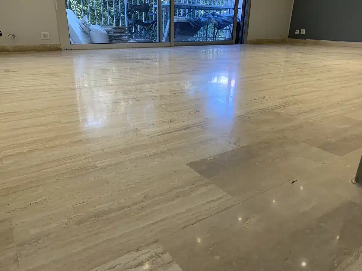 travertin-poli-satine-salon-grasse Salon d'un appartement de Grasse avec un sol en travertin poli-satiné, reflétant la lumière de la baie vitrée et, au premier plan, les spots du plafond