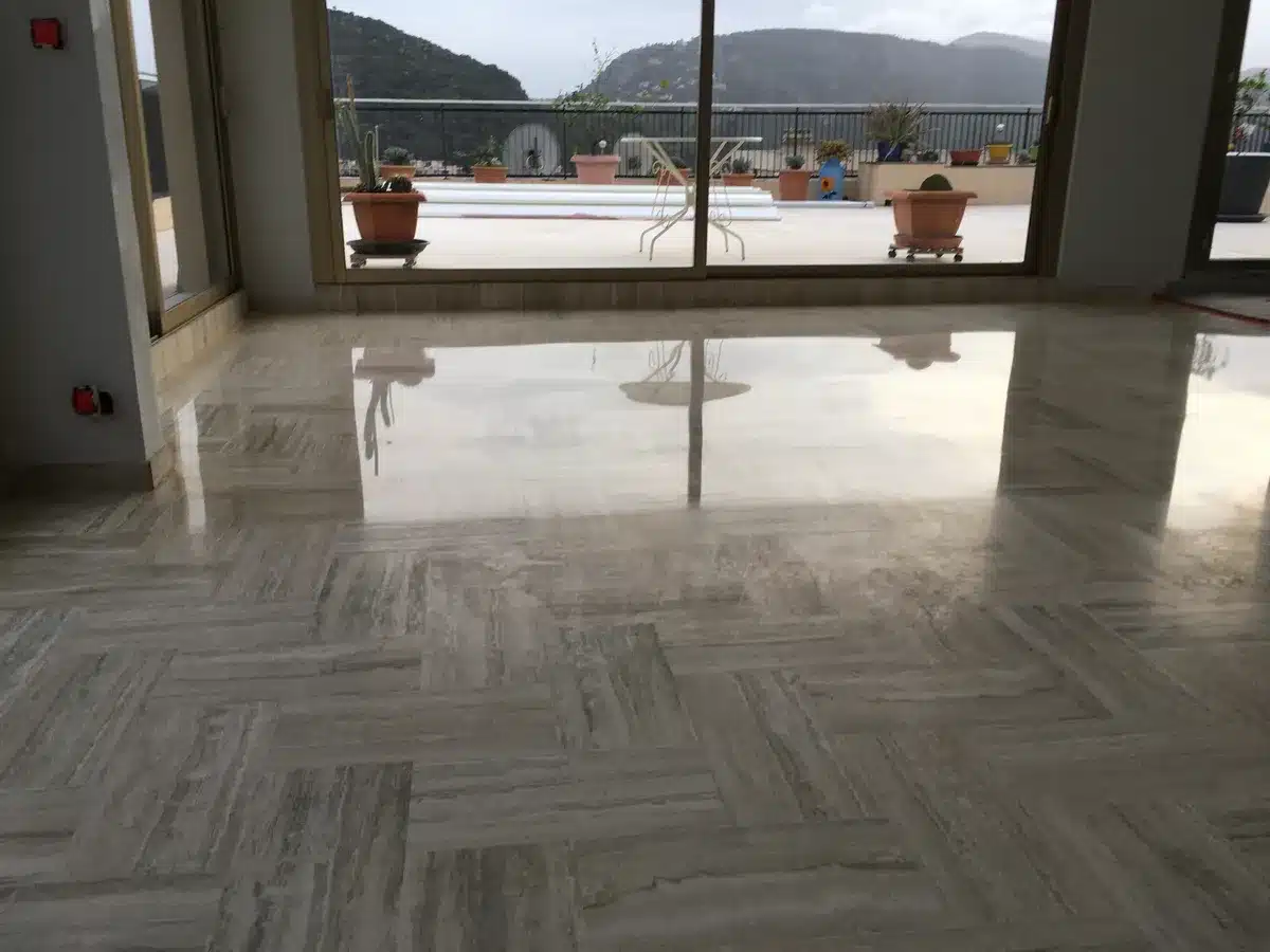 travertin-premiere-zone-poli-brillant-penthouse-mandelieu Sol en travertin d'un penthouse à Mandelieu-la-Napoule : la première zone en poli-brillant reflète la baie vitrée, le reste du sol n'est pas encore lustré